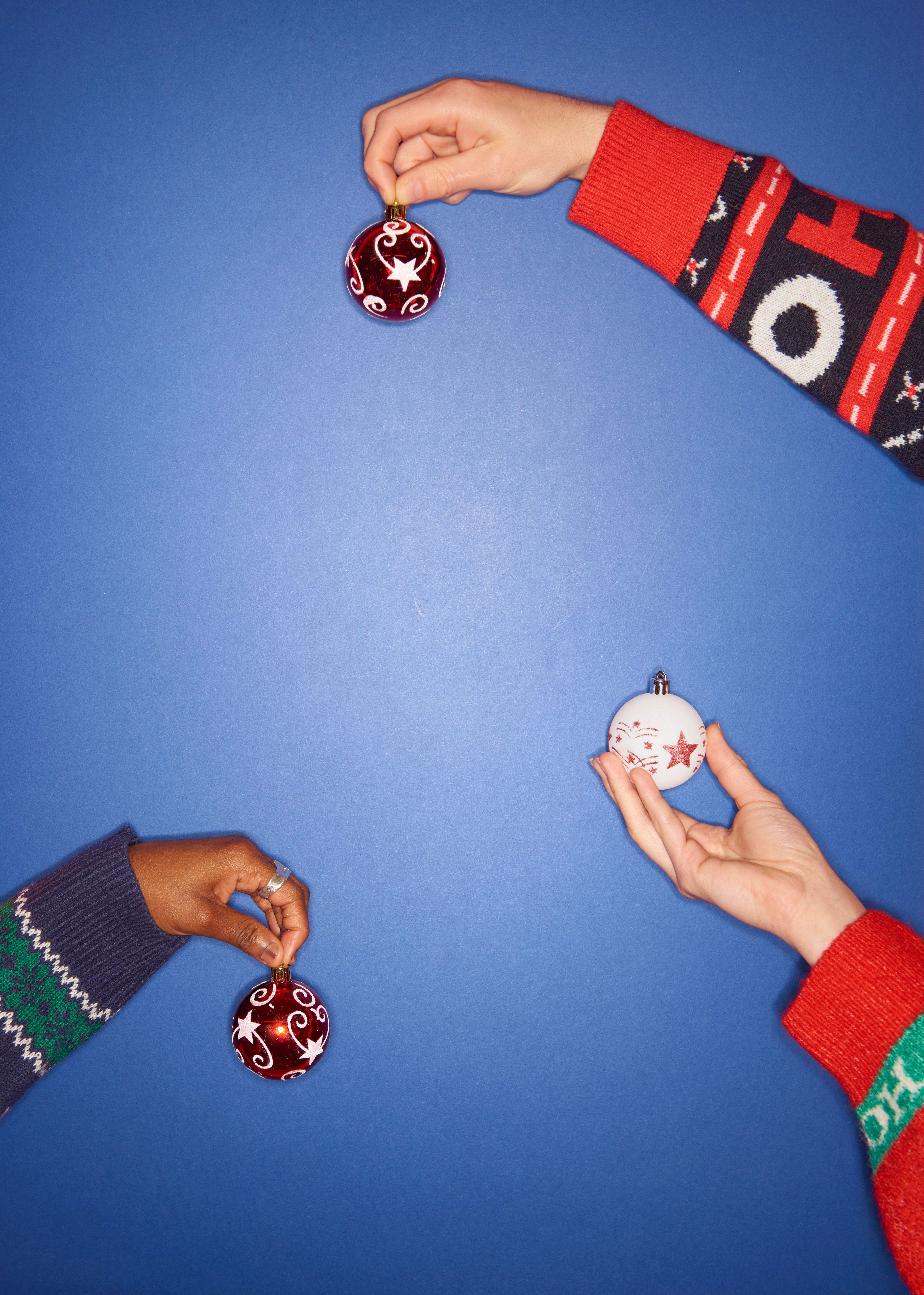 Tre hender som holder festpynt mot en blå bakgrunn, hver iført en annen mønstergenser