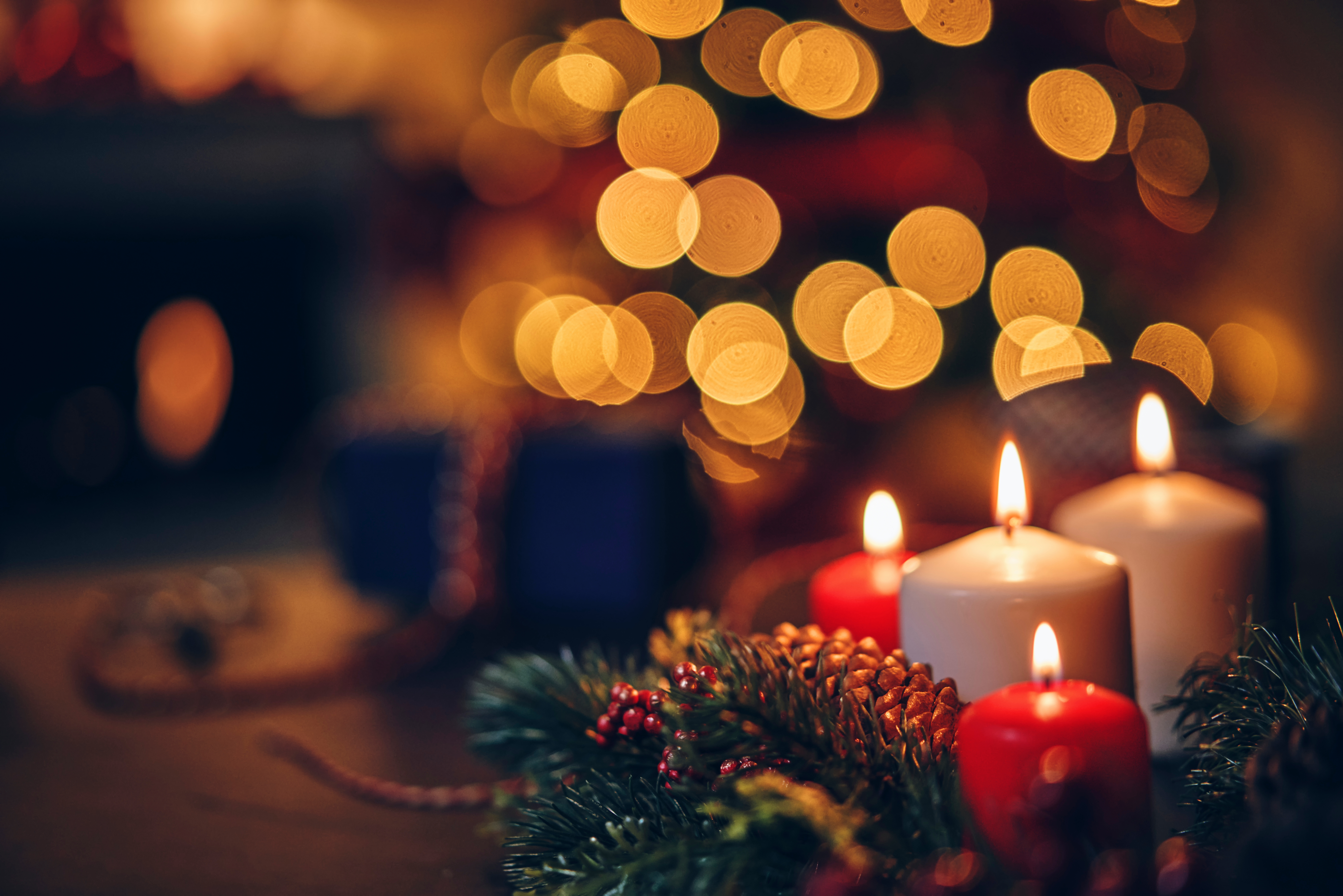 Stearinlys og kongledekorasjoner med et uskarpt juletre i bakgrunnen, skaper en varm, festlig atmosfære