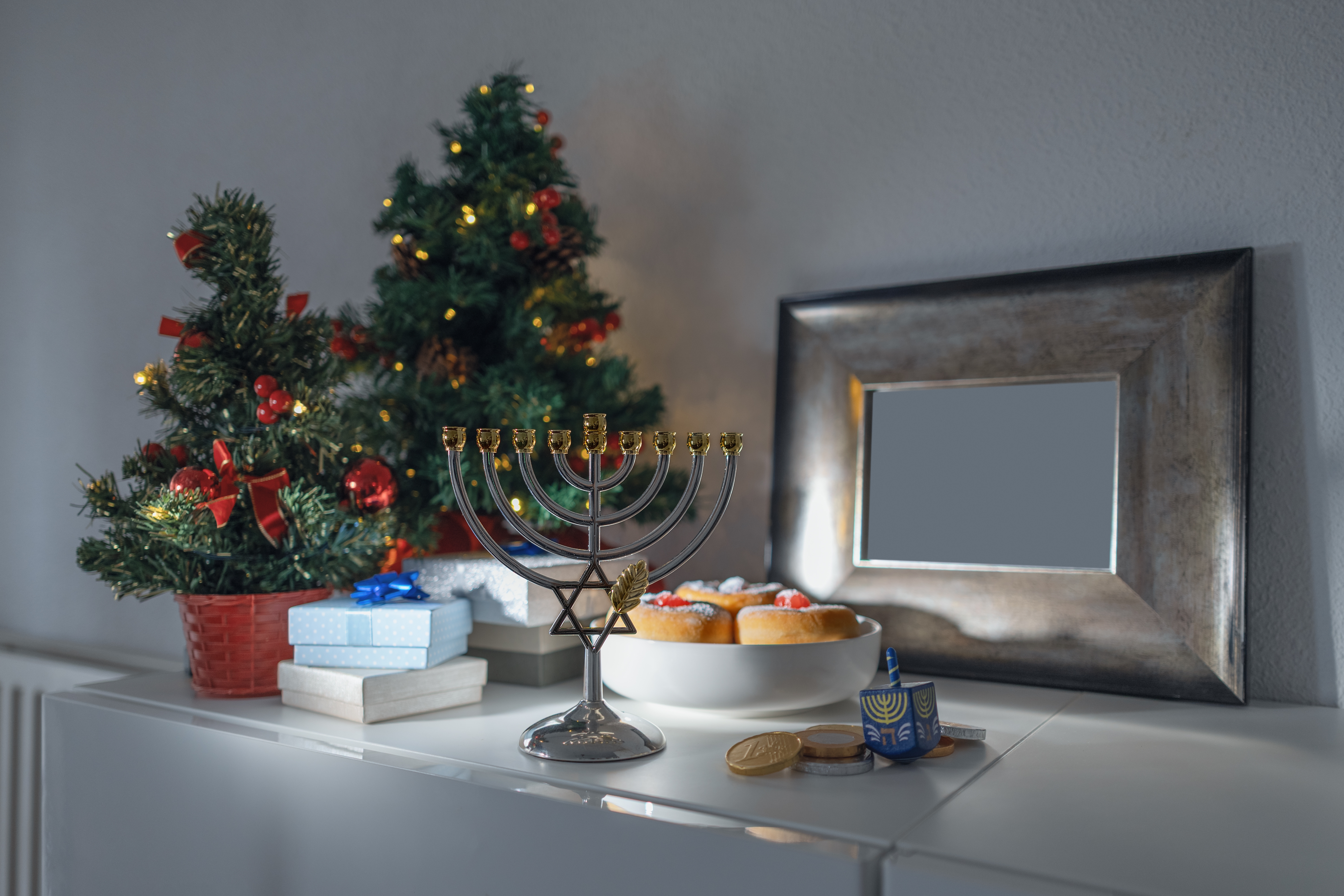 Feriescene med en tent menora, små dekorerte trær, gaver, dreidel og smultringer på en hvit overflate