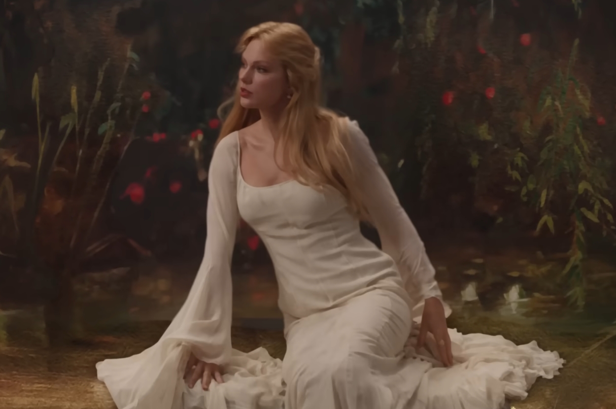 Taylor Swift in flowing, ethereal dress sits gracefully on the ground, looking contemplative, with a soft-focus, natural background in "Fate of Ophelia" music video