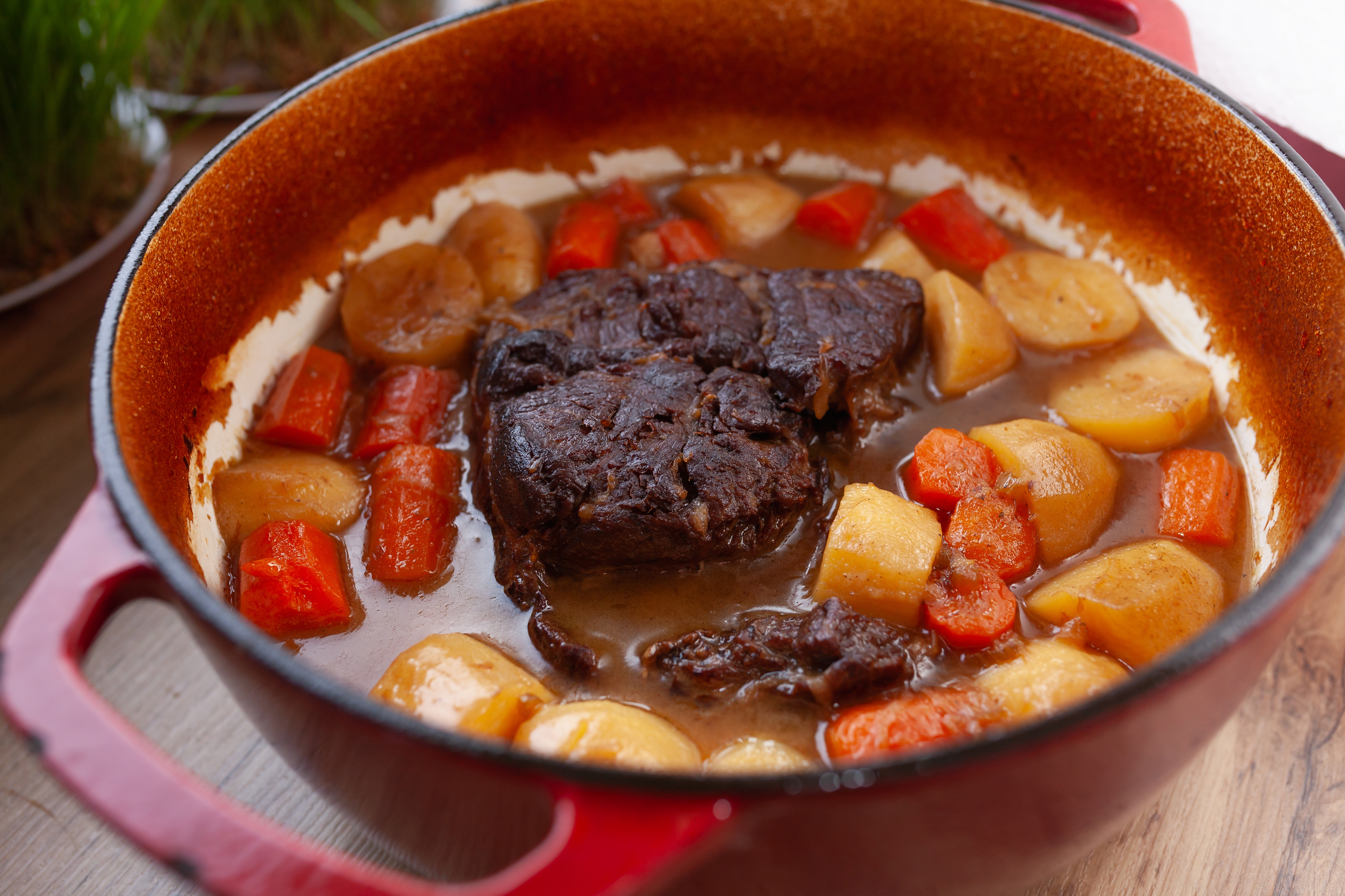 A hearty beef stew with carrots and potatoes in a red pot, showcasing a rich and savory dish perfect for cozy meals