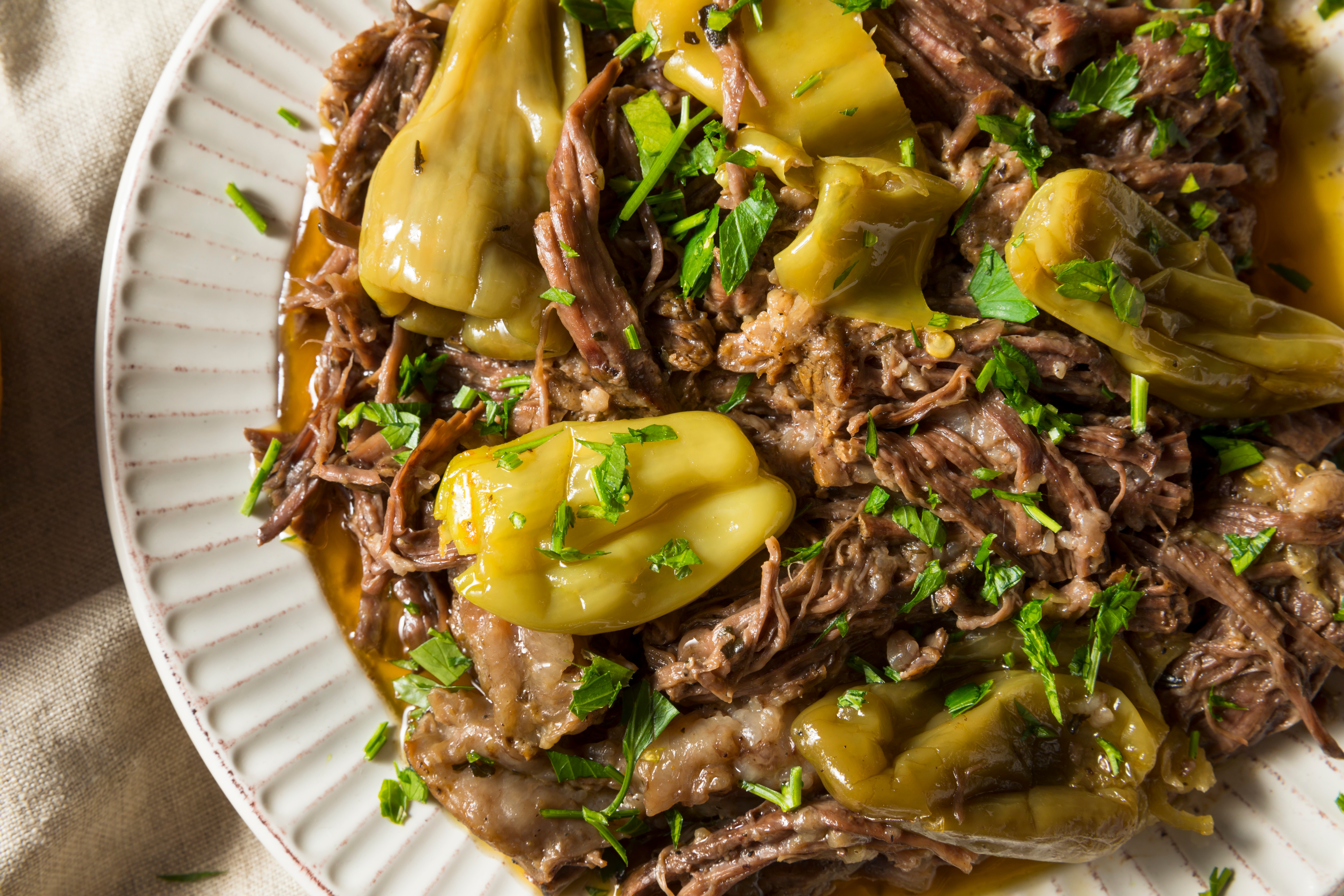 A plate of pulled beef roast topped with pepperoncini and garnished with parsley