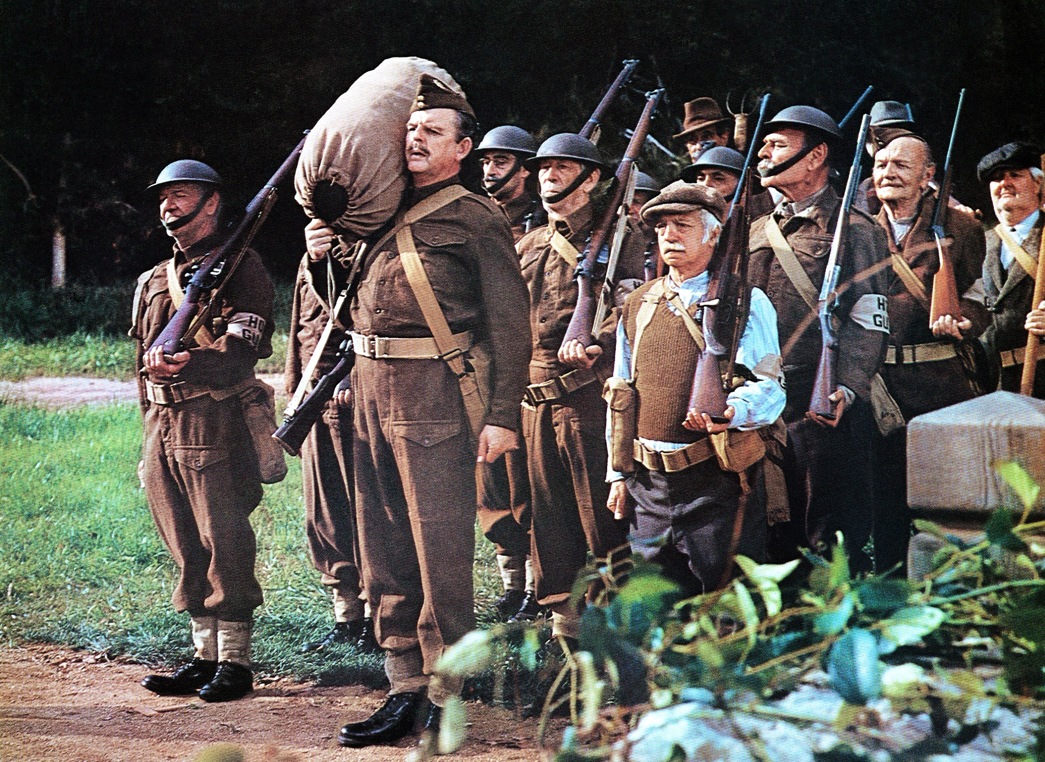 A radical  of actors dressed arsenic  WWII soldiers march successful  formation, carrying rifles and a ample  sack, depicting a vintage subject   scene