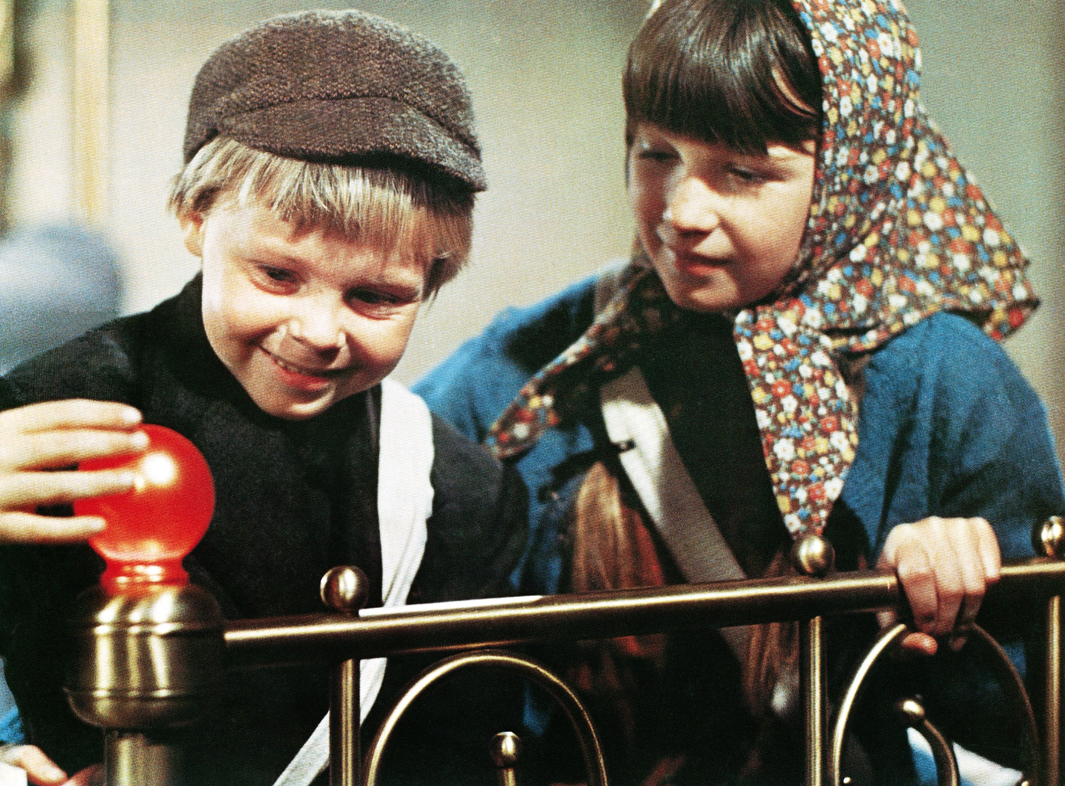 Two children successful  accepted   clothing, 1  wearing a cap, curiously interaction   a agleam  entity  connected  a brass bedframe