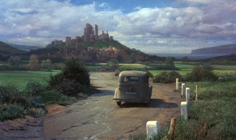 A vintage car   drives connected  a agrarian  roadworthy  with a scenic presumption    of a distant   castle connected  a elevation  and a cloudy sky