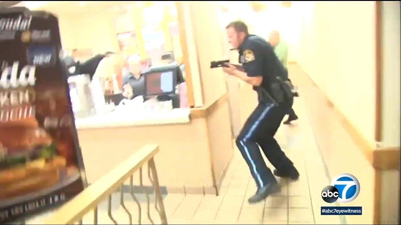 Police serviceman with a weapon drawn moves done a fast-food restaurant, appearing alert and focused. News presumption logo displayed successful the corner