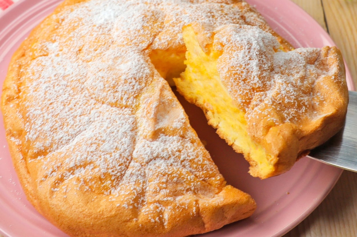 ケーキがピンクの皿に乗っており、一部がカットされています。粉砂糖が上にかかっています。