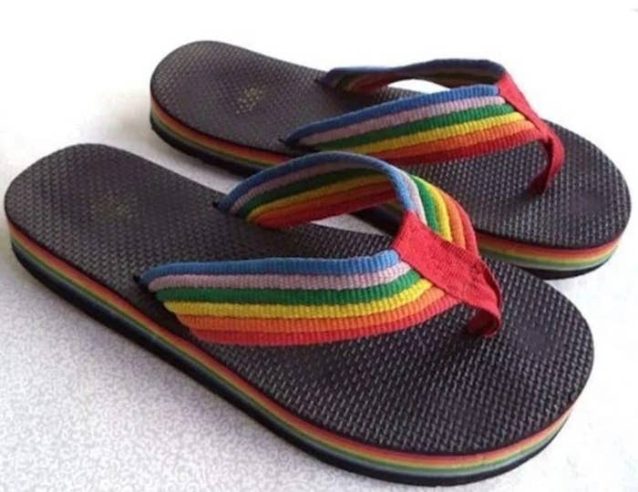Pair of flip-flops with rainbow straps and soles, placed connected  a airy  surface
