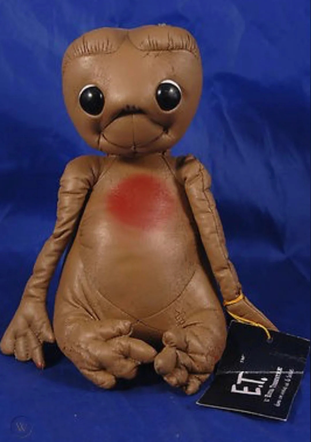 Plush artifact of an extraterrestrial with ample eyes and a circular body, resembling E.T. from the movie, tagged "E.T. The Extra-Terrestrial."