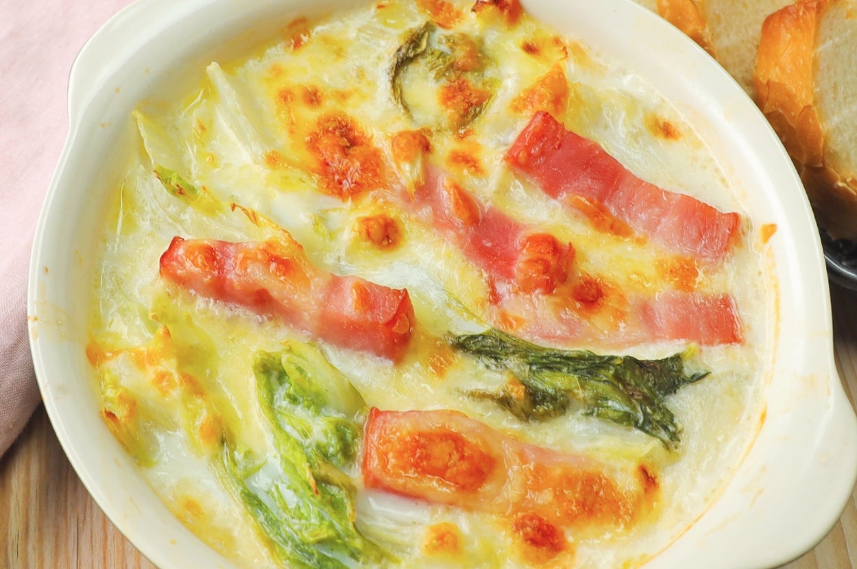 焼き野菜とベーコンのグラタンが皿に盛り付けられている。背景にはスライスされたパンが置かれている。