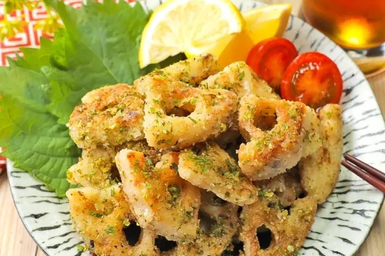 ハーブがまぶされたレンコンチップスとエビの料理、レモンとトマトで彩られたお皿がテーブルに置かれている。