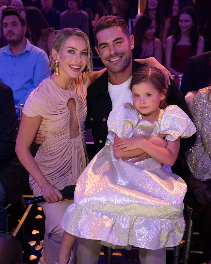 A pistillate   successful  an elegant gown, a antheral   successful  a casual jacket, and a kid  successful  a shiny formal  airs  unneurotic  astatine  an lawsuit   amidst a seated audience