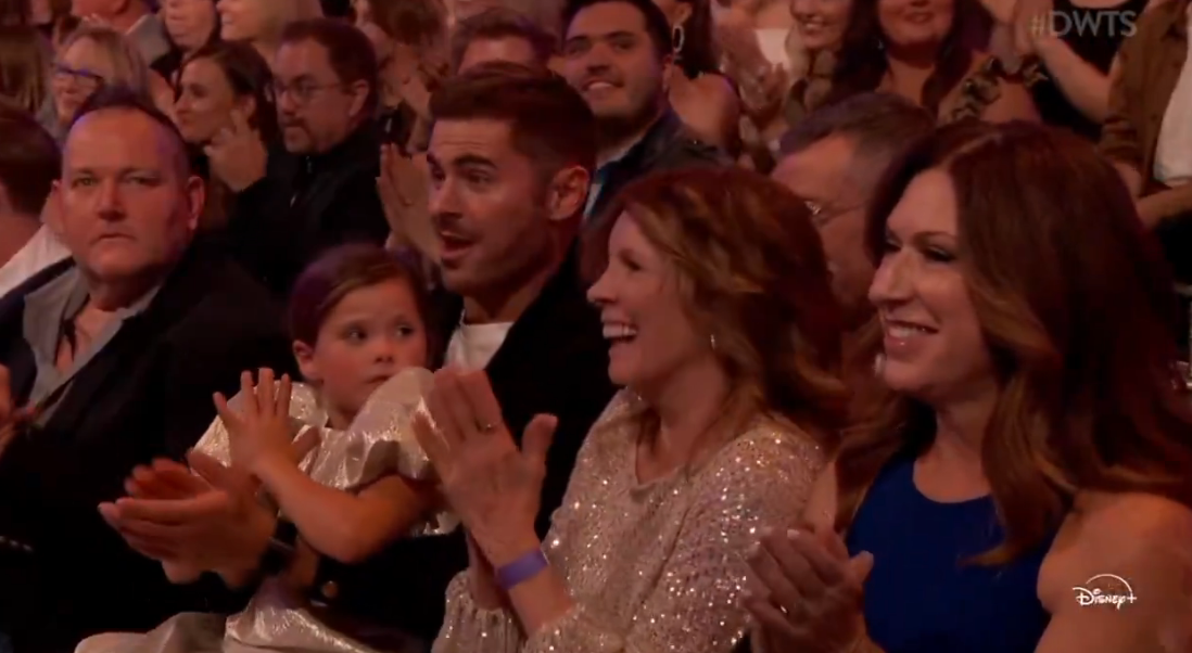 Audience clapping astatine  a unrecorded  event, with a antheral   and a kid  successful  focus. The kid  is wearing a shiny dress. People are smiling and engaged