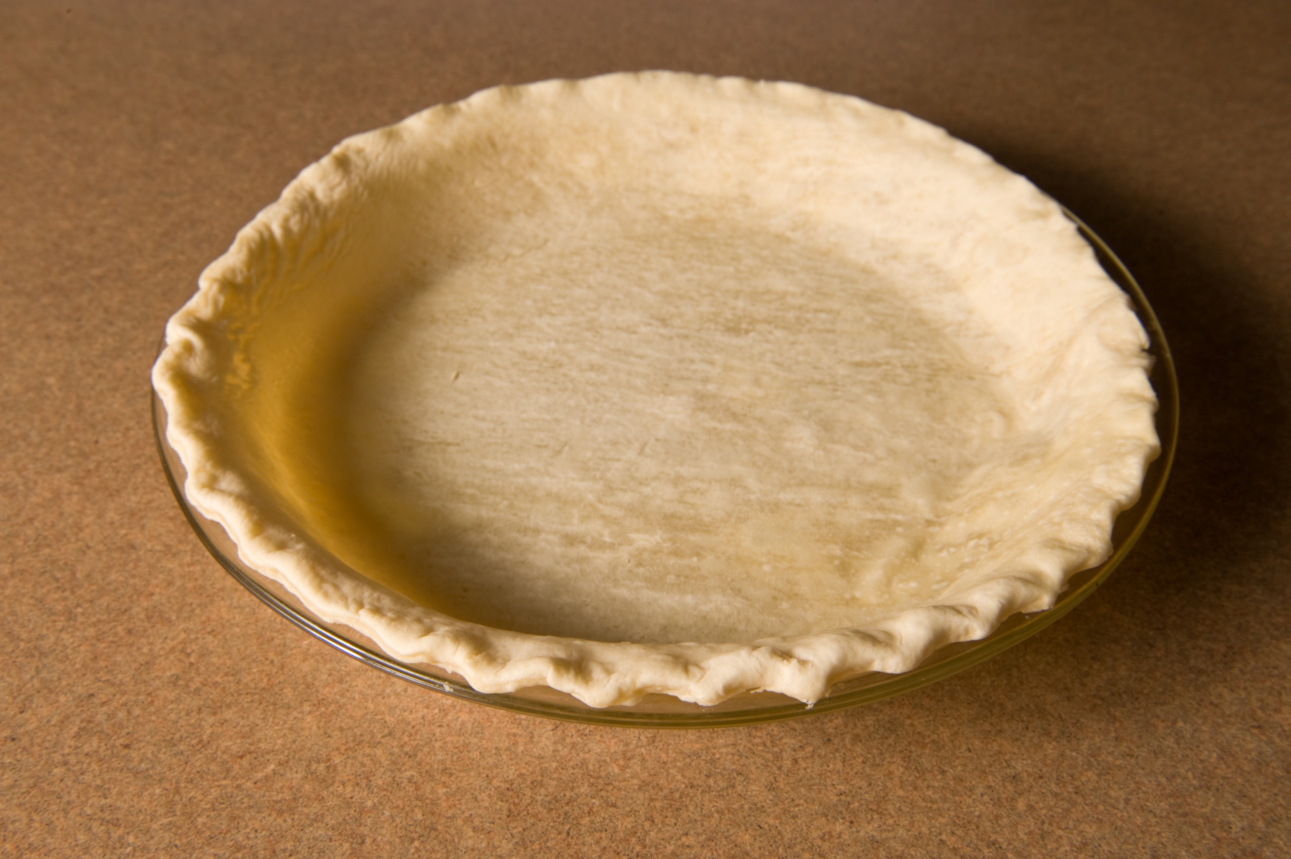 Empty pie crust in a glass dish on a countertop, ready for baking