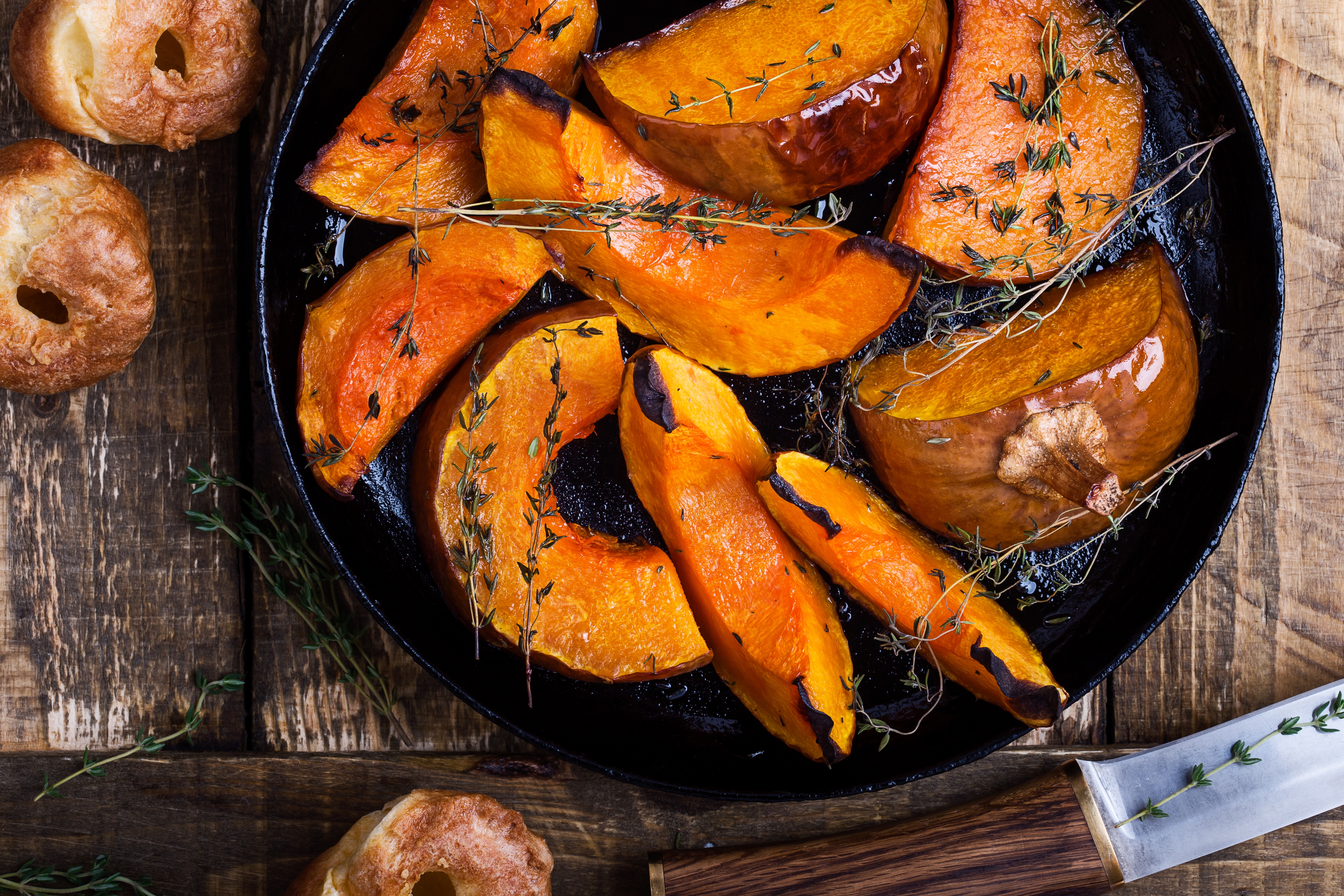 Roasted pumpkin slices with herbs in a pan, surrounded by a few small apples and a knife on a wooden surface