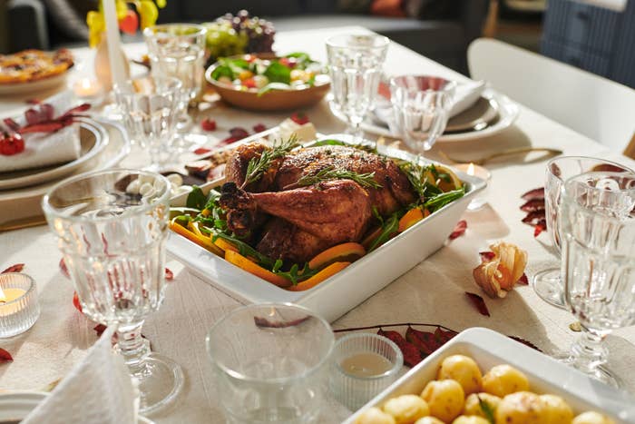 A holiday table setting features a roasted turkey with garnishes, crystal glasses, side dishes, and decorative autumn leaves