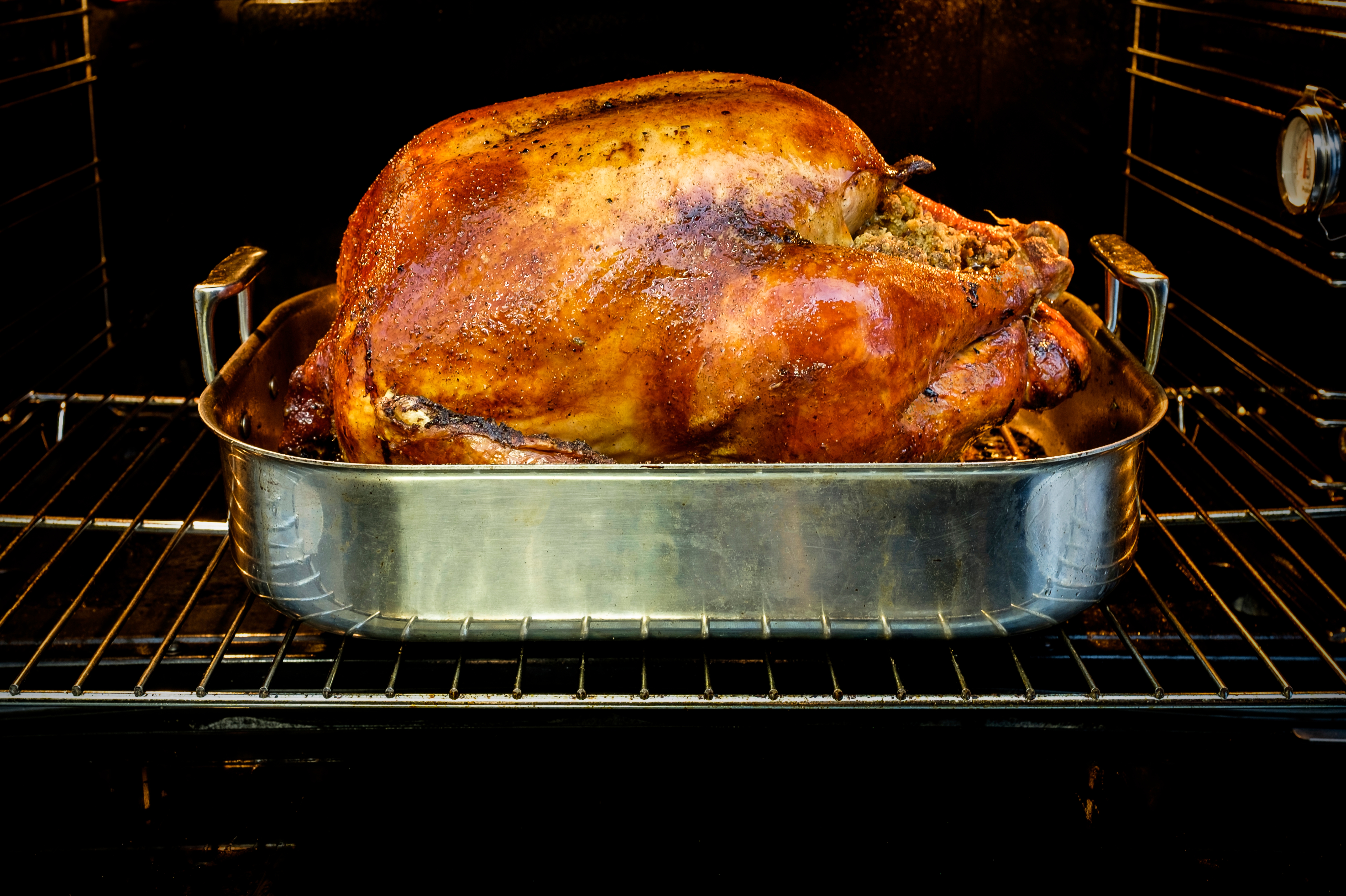 Turkey roasting in a metal pan inside an oven. The turkey appears to be fully cooked with a crispy exterior