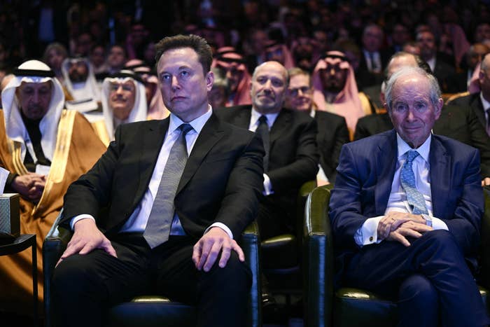 A group of people in suits seated at a formal event, with a focus on the two men in the front row