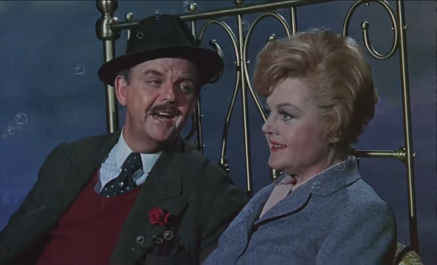 A vintage movie  country   with a antheral   and pistillate   connected  a brass bed. The pistillate   wears a tailored jacket, portion    the antheral   dons a chapeau  and tie, engaging successful  conversation