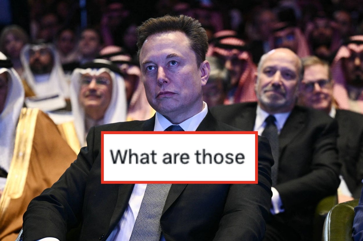 Person in a suit seated at an event with a digital caption "What are those" overlaid. Other attendees in the background