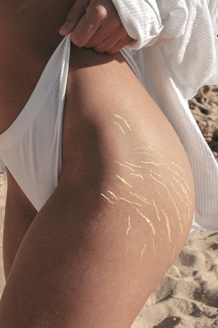 Close-up of a person&#x27;s thigh with agelong   marks highlighted successful  gold. They are astatine  the beach, wearing a achromatic  swimsuit and shirt