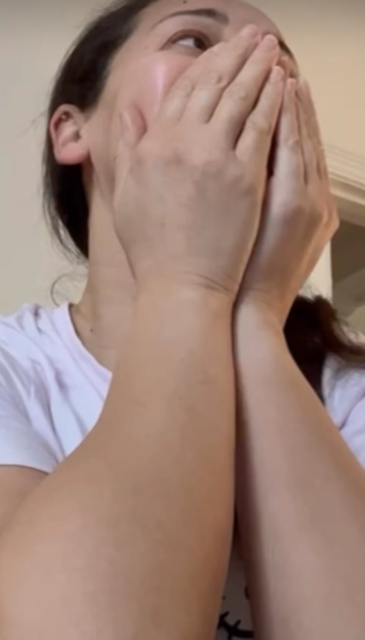 Person i en t-skjorte som dekker munnen med begge hender, virker overrasket eller emosjonell