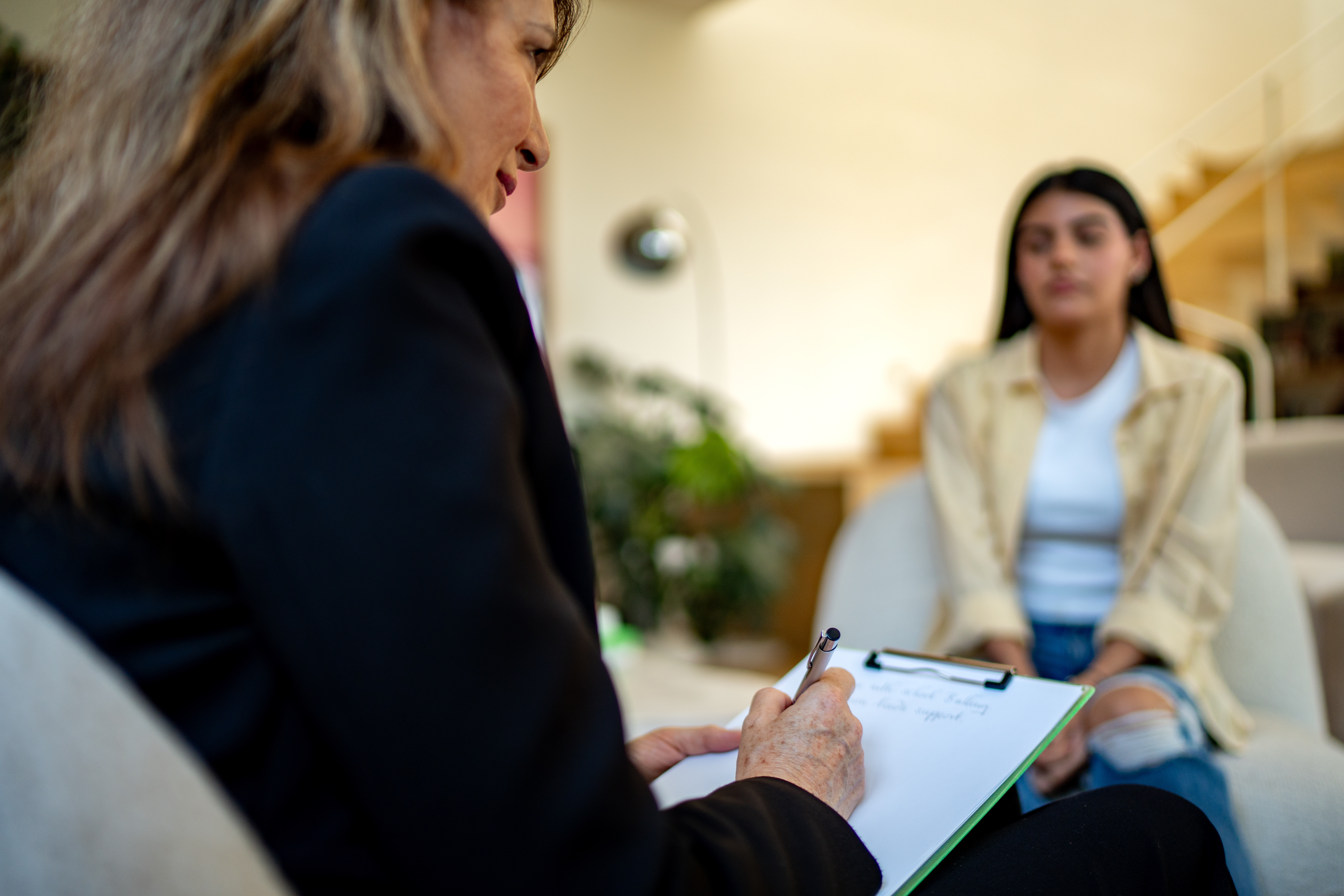 Person som holder utklippstavle og penn, snakker med en annen person i uformelle klær, foreslår en veiledning eller intervju i en avslappet setting