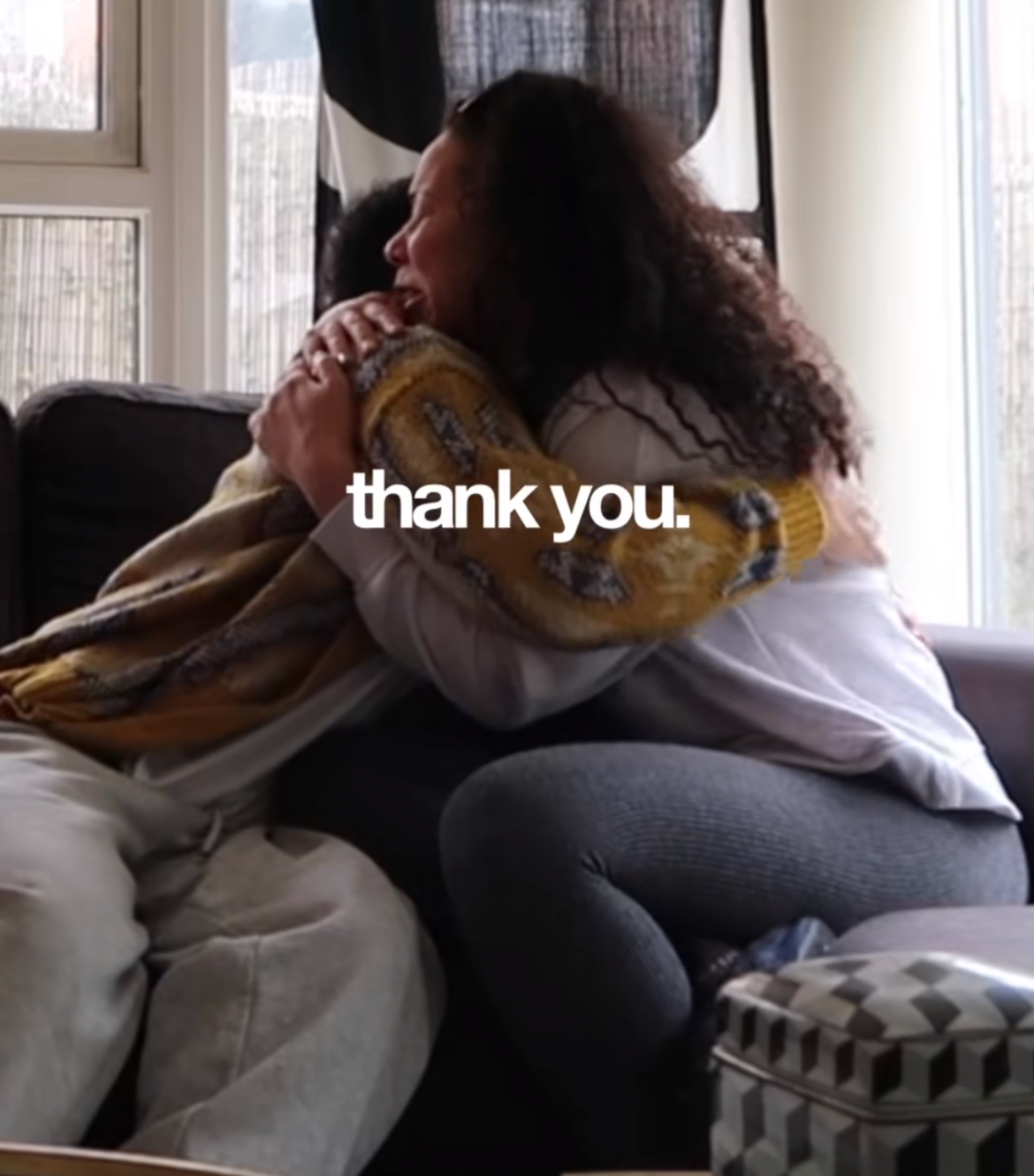 To personer deler en hjertelig klem på en sofa med "takk." lagt på bildet, og formidler takknemlighet og varme