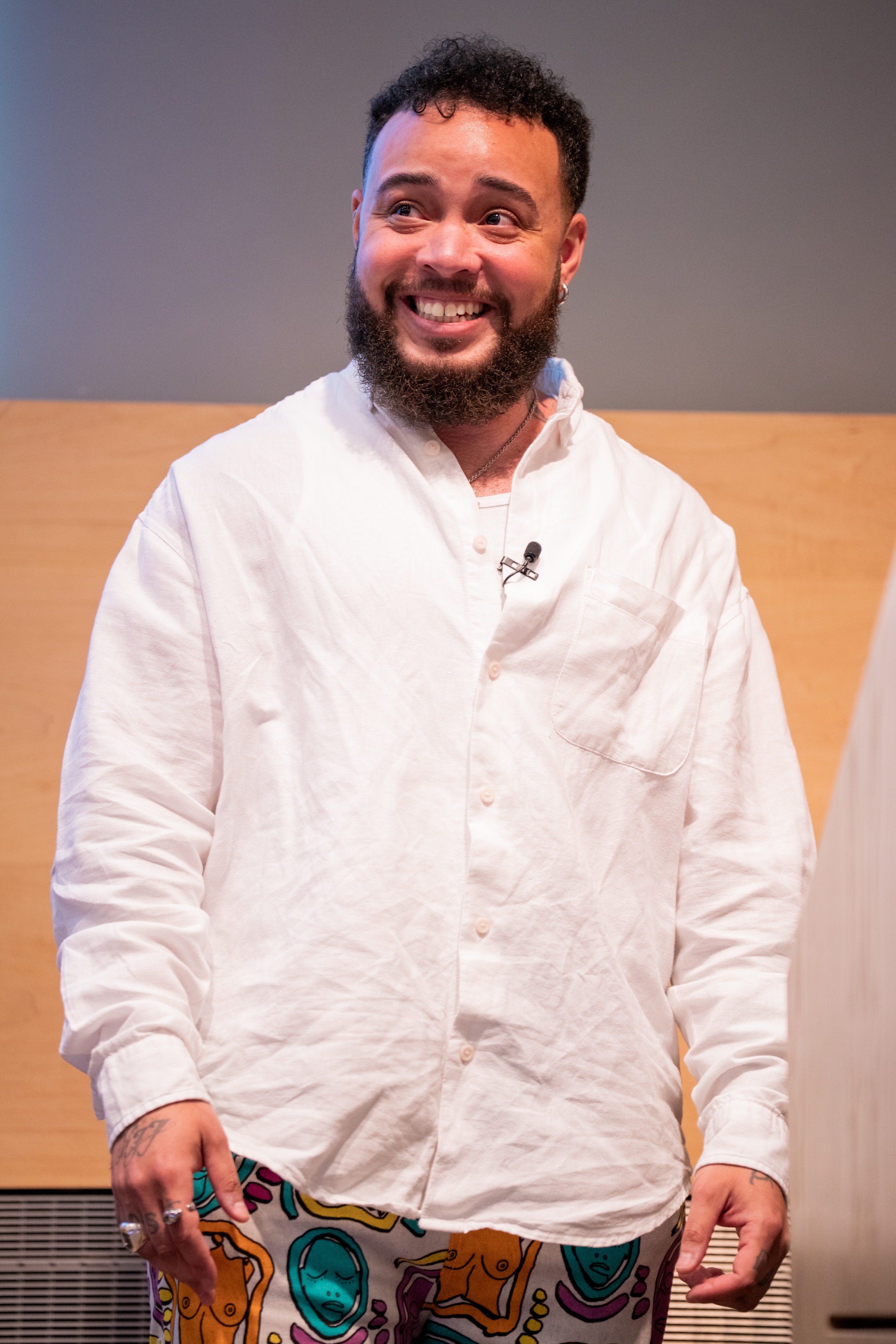 Person som smiler, iført en uformell hvit skjorte med knapper og trykte bukser med abstrakt design