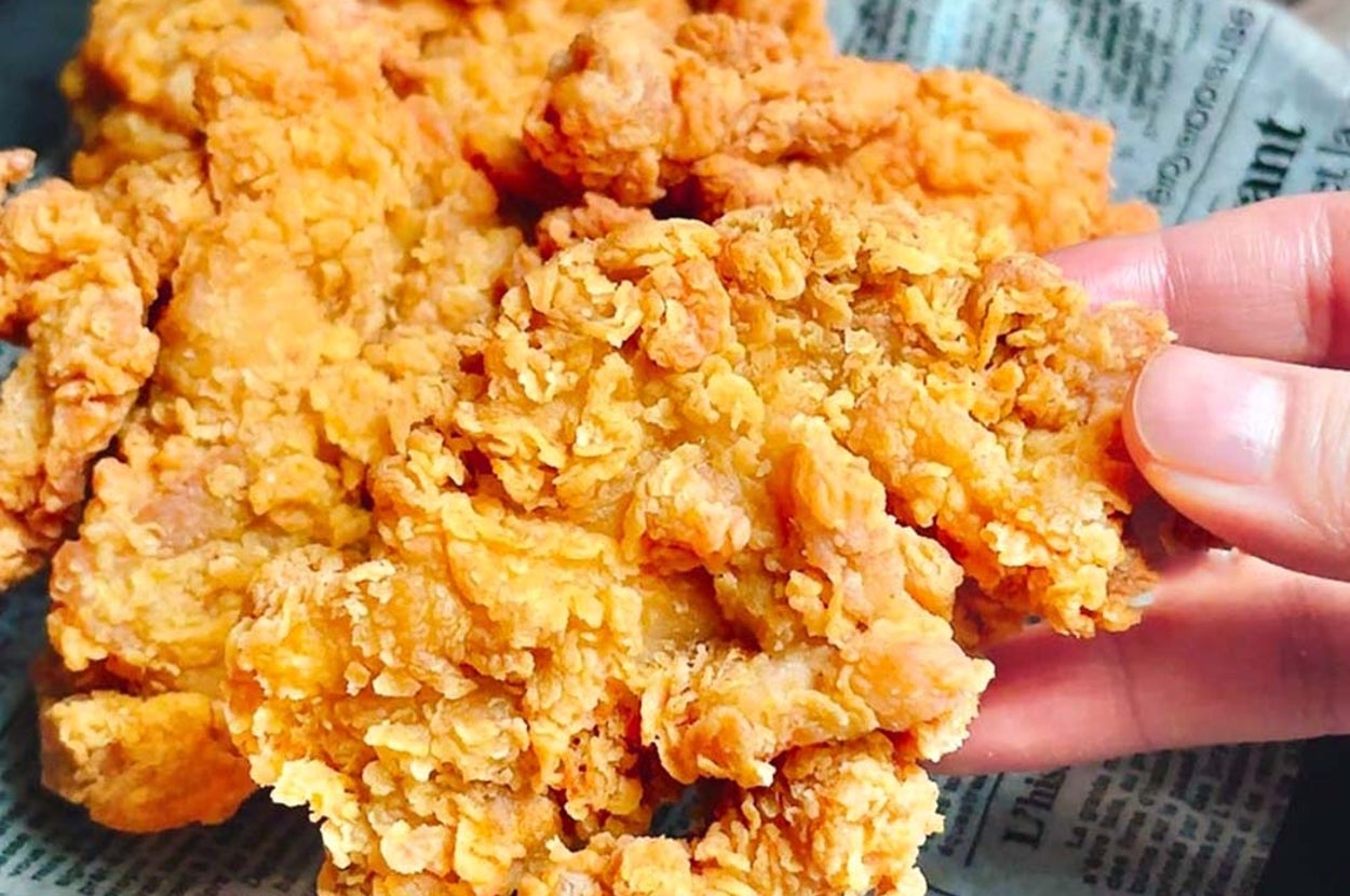 手で持たれたフライドチキンの盛り合わせが新聞紙の上に置かれています。