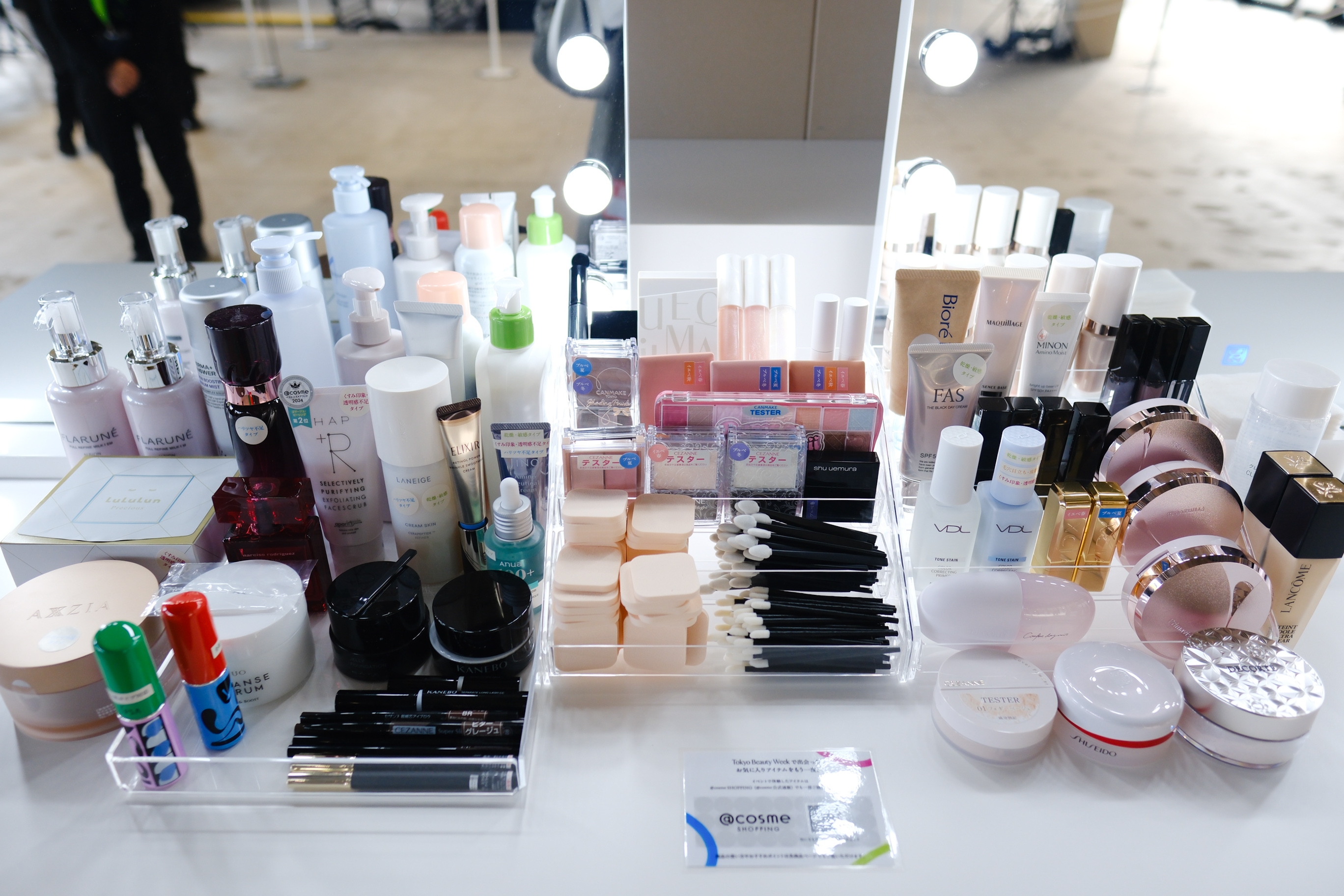 化粧品が多数並べられたテーブル。スキンケア製品、リップクリーム、メイクブラシが含まれている。