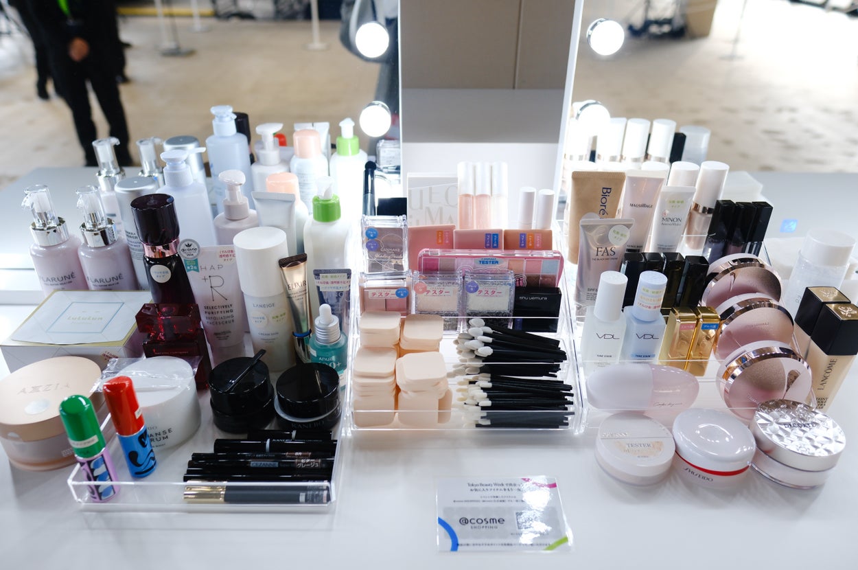 化粧品が多数並べられたテーブル。スキンケア製品、リップクリーム、メイクブラシが含まれている。