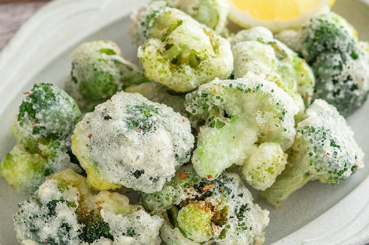 ブロッコリーの天ぷらが白い皿に盛られている。横にレモンのくし切りが添えられている。