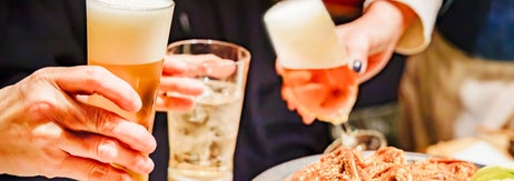 食事の場でビールや料理を囲み、乾杯する数人の手。