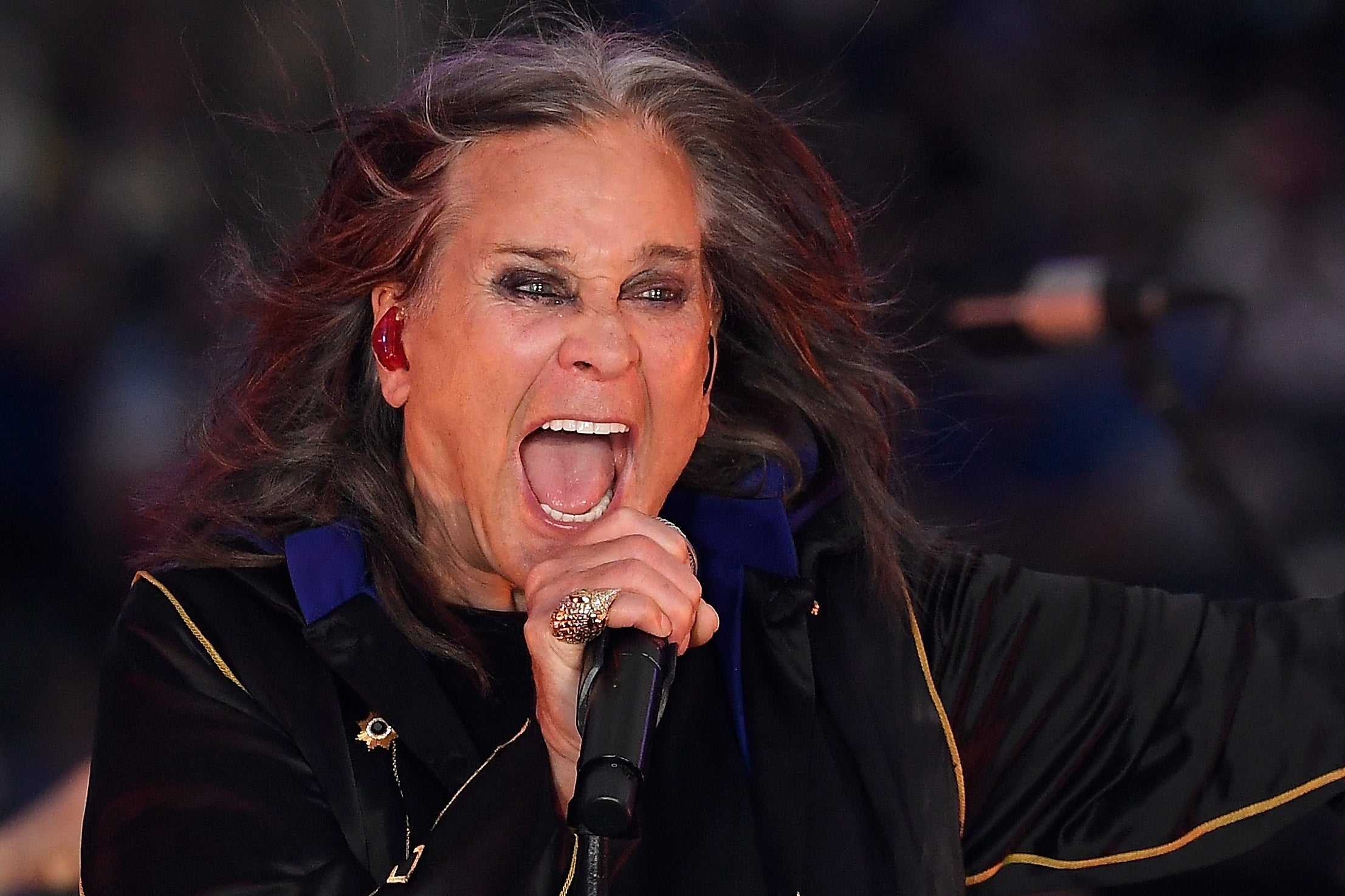 Person passionately singing on stage in a dark, embellished coat during a live performance