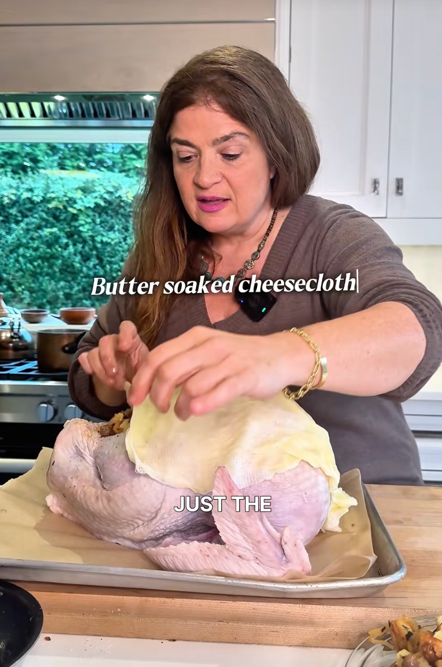 Alex Guarnaschelli covers a turkey with a butter-soaked cheesecloth in a kitchen setting