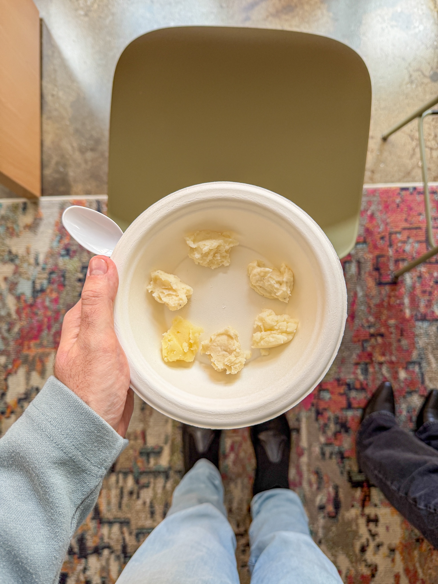 Person holding a bowl with several scoops of ice cream inside, viewed from above, with a patterned rug and chair in the background