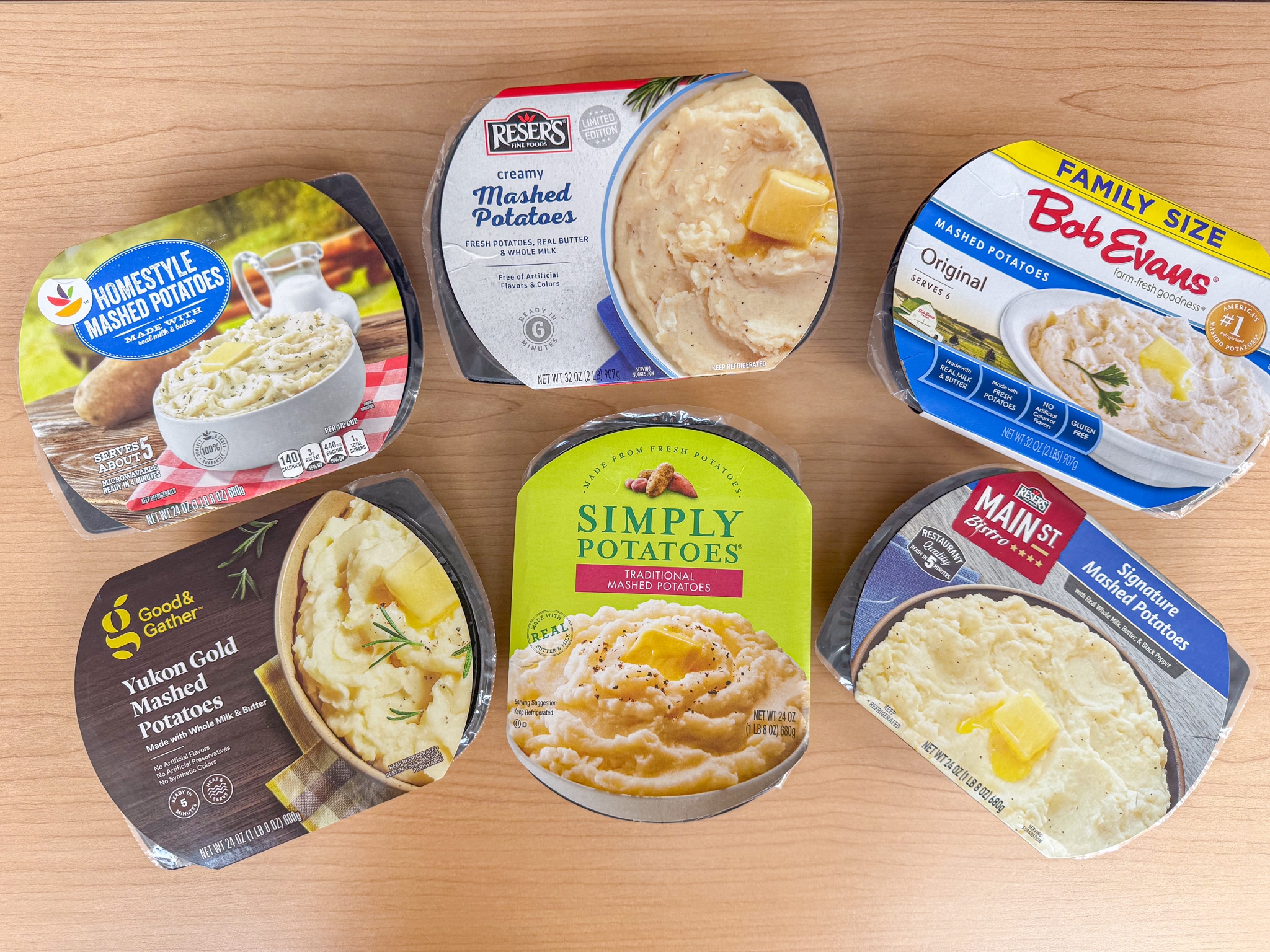 Six containers of mashed potatoes from various brands are arranged on a table, showcasing different packaging designs
