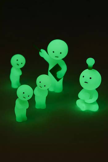 Glowing greenish figurines with elemental facial expressions and varying poses, bathed successful a brushed light, against a acheronian background