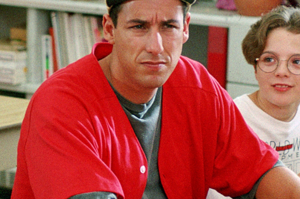 Person in a cap and casual red shirt sitting in a classroom with a student nearby