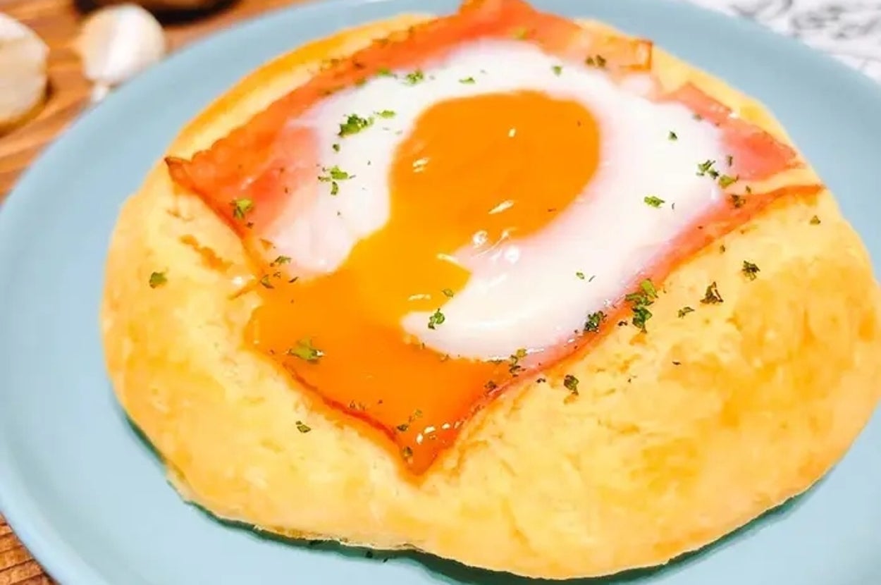 お皿の上にパン、ハム、目玉焼きが乗っている料理。背景ににんにくと新聞が見える。