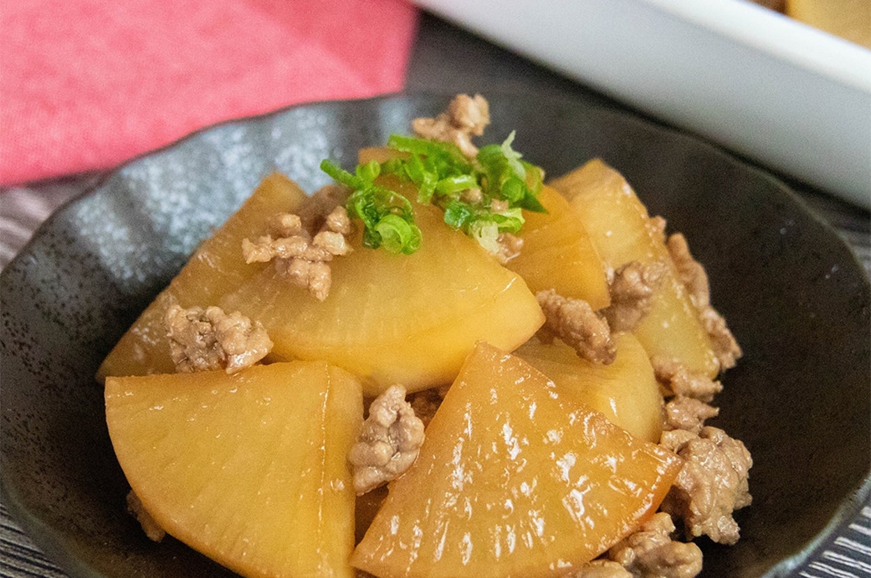 大根と挽き肉を使った大根のそぼろ煮の料理が黒い皿に盛り付けられている。上に刻んだ青ネギがトッピングされている。