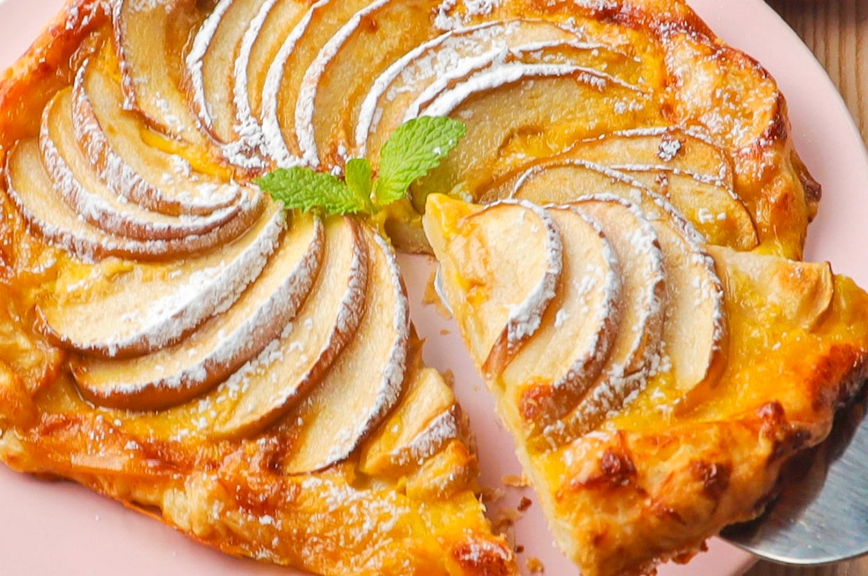 焼きたてのアップルガレットがピンクの皿に載っている。スライスされたリンゴが美しく並べられ、粉砂糖がかかっている。