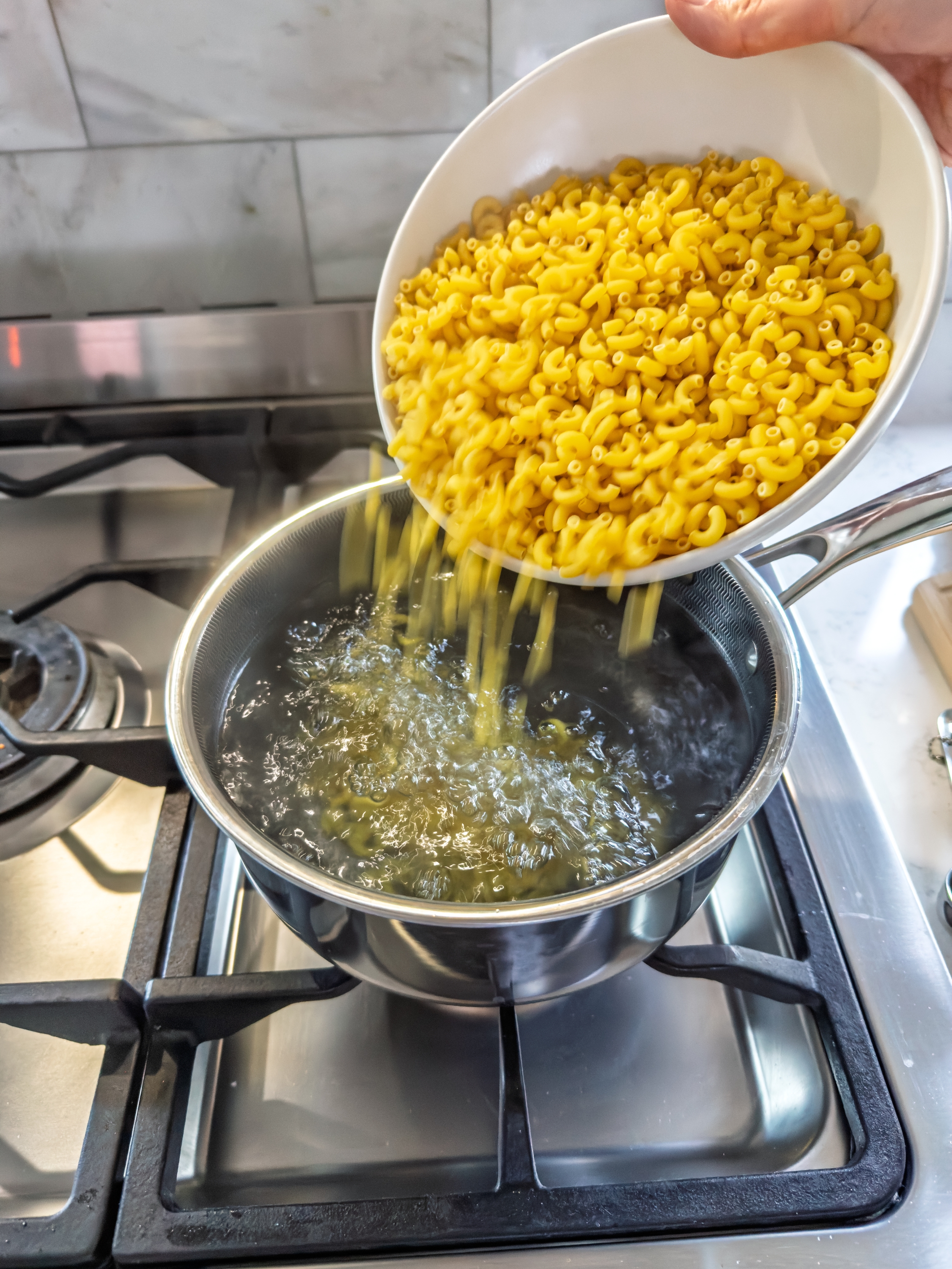 Pasta being poured from a bowl into boiling water on a stove