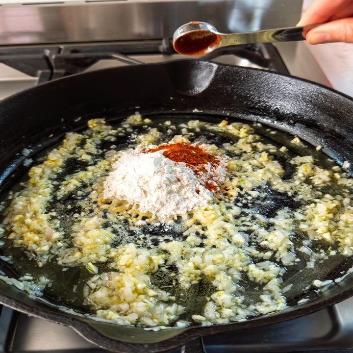 Garlic and flour cooking in a skillet, with a hand adding a spoonful of spice