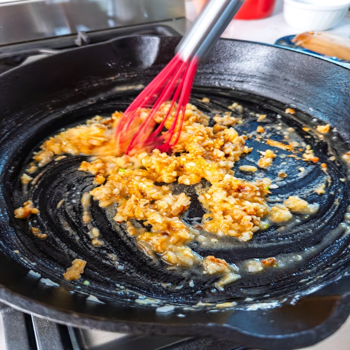 Onion and garlic being sautéed in a cast iron skillet with a red whisk