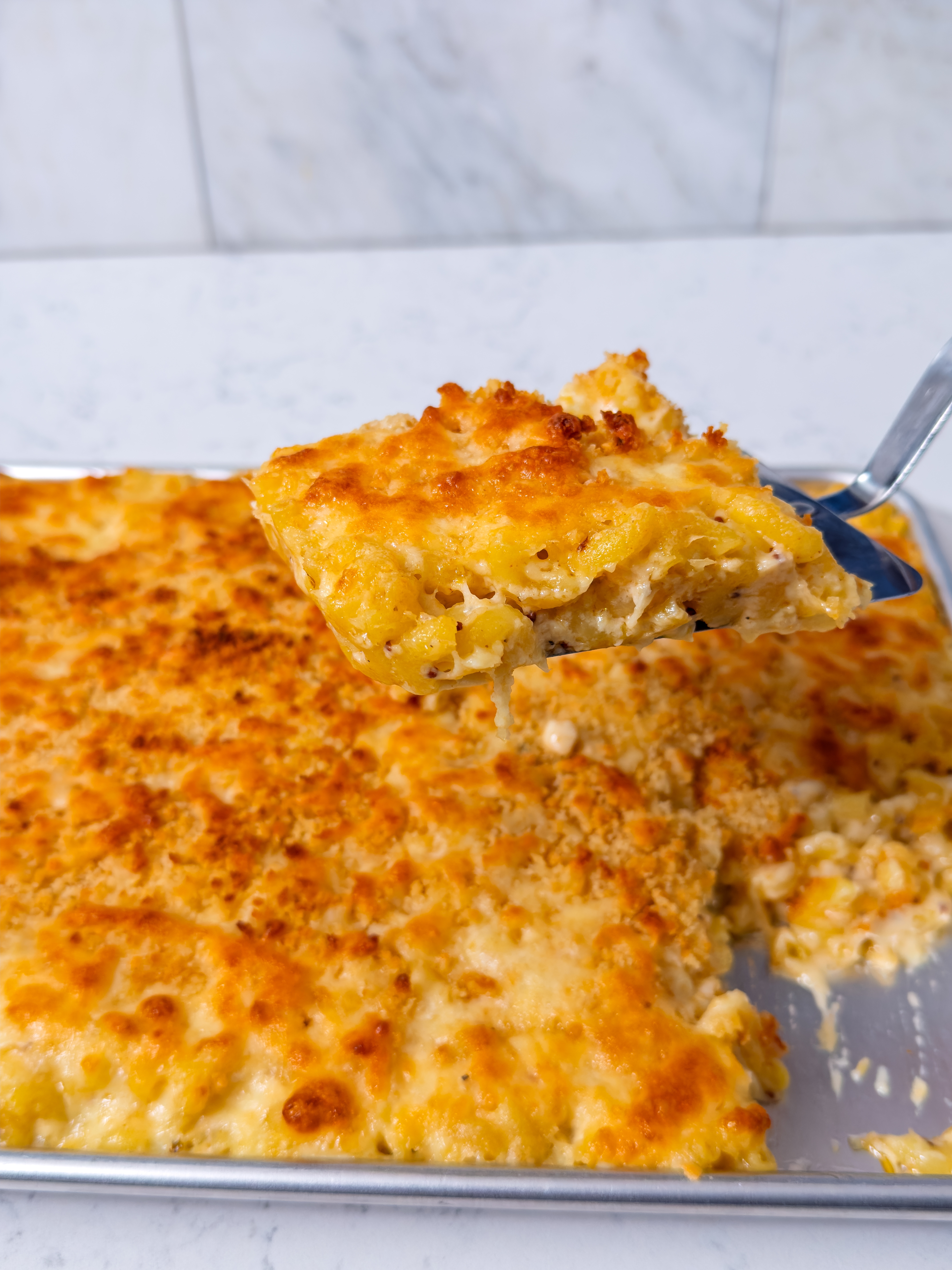 Cheesy baked macaroni and cheese being served from a baking dish, featuring a crispy top layer