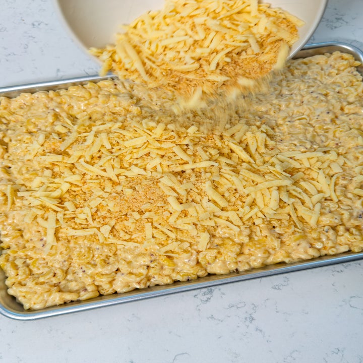 Grated cheese being poured onto a tray of creamy mac and cheese, ready for baking
