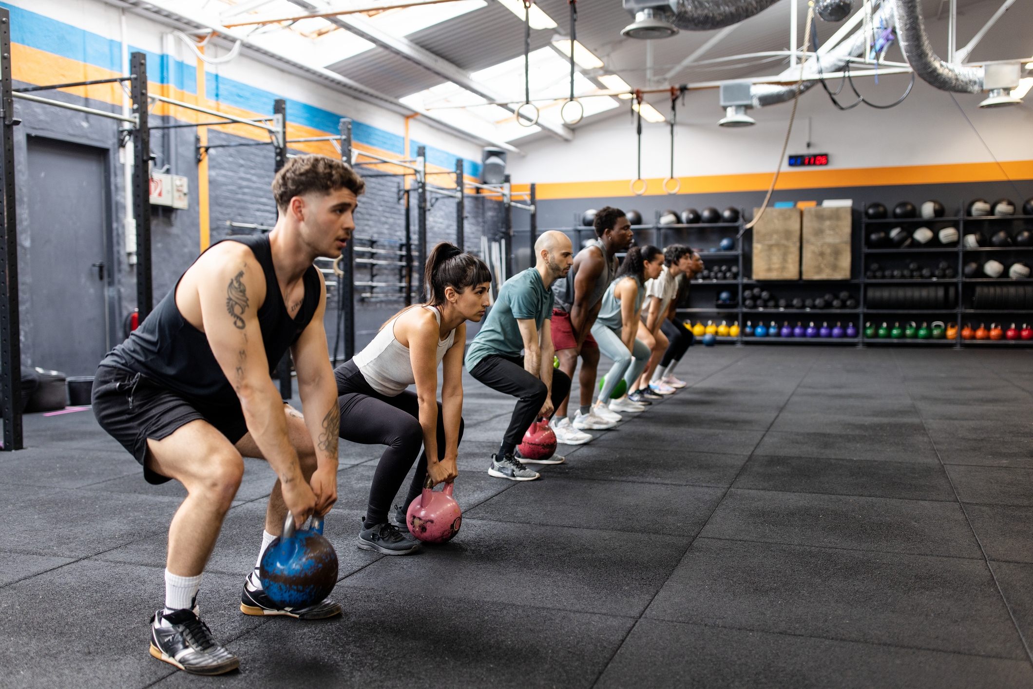 Folk i en gymtime som gjør kettlebell-øvelser, plassert på rad med fokuserte uttrykk, viser teamarbeid og treningsdedikasjon