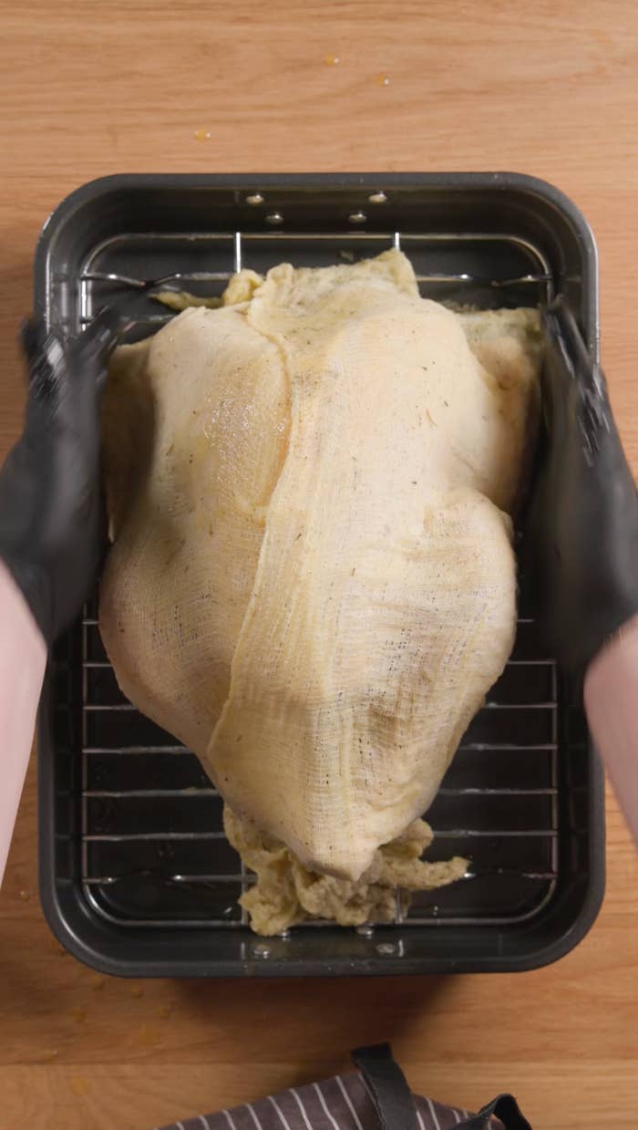 Person preparing a turkey in a roasting pan with gloved hands, on a wooden surface
